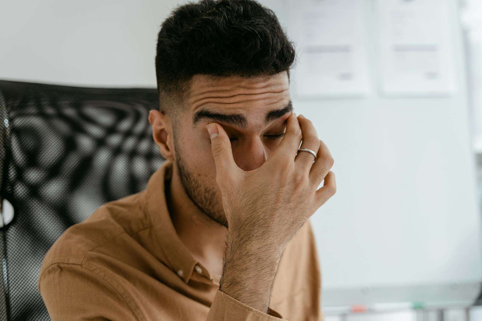 a man in brown polo shirt touching his eyelids